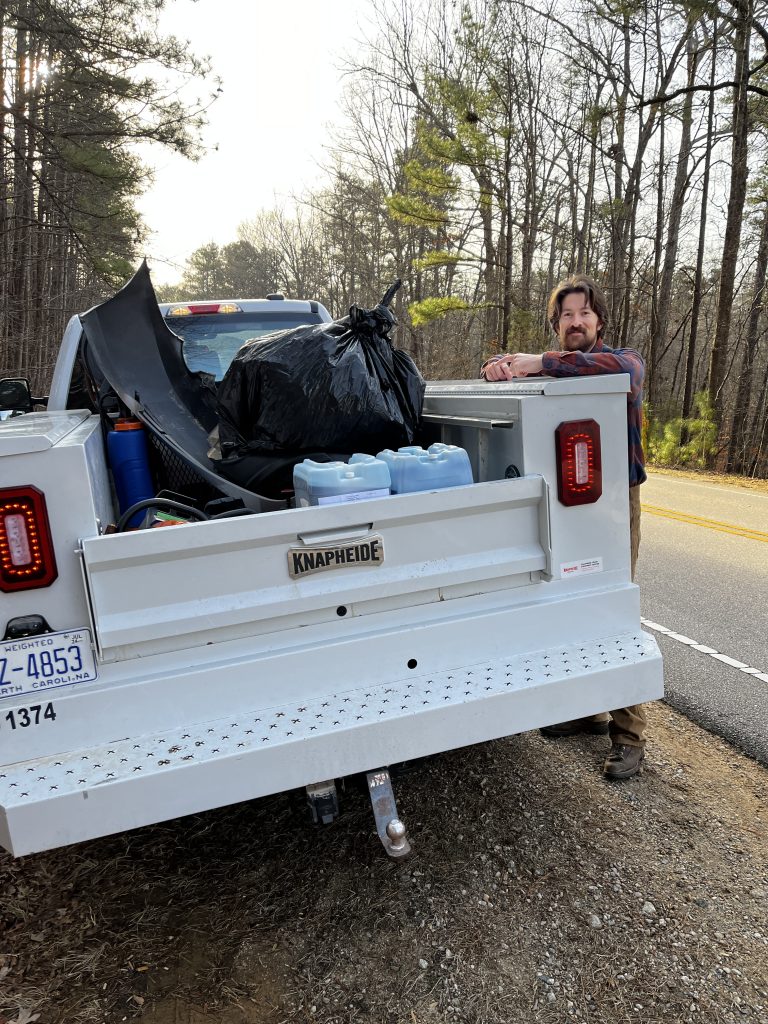 Zach standing next to a truck loaded with tools and a large trashbag